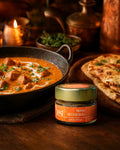 A ZEST Indian Butter Bliss spice blend jar displayed next to a rich butter chicken or paneer dish and naan bread on a dark wooden table, with candlelight in the background.