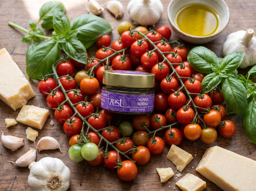 Nonna Norma spice blend jar surrounded by cherry tomatoes on the vine, basil, garlic, Parmesan and olive oil on a rustic wooden table